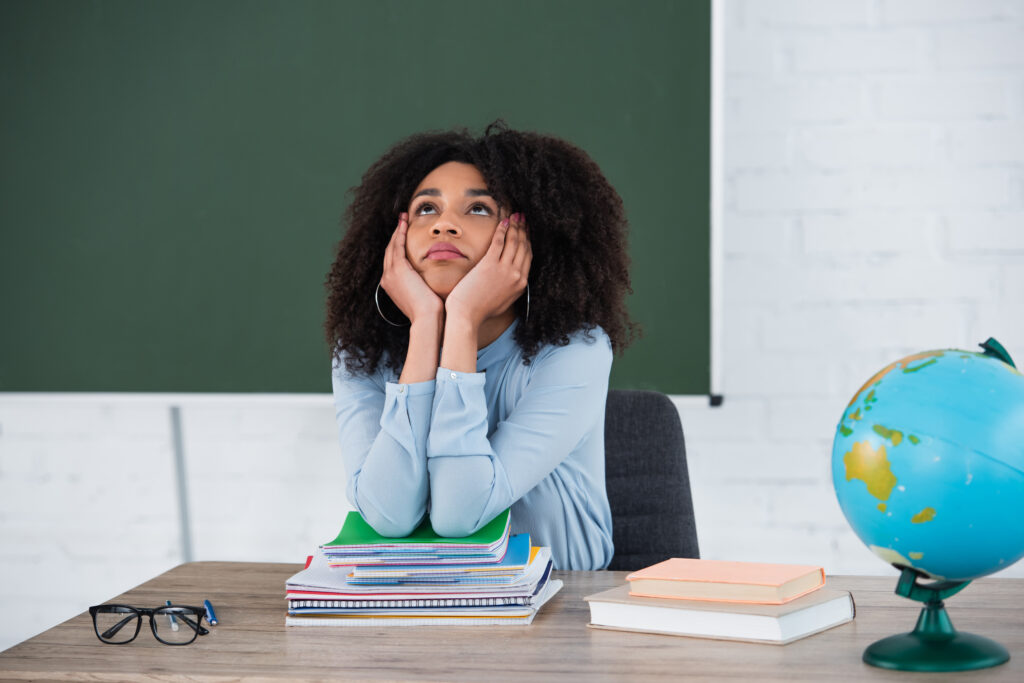 A pensive young high schooler student looks up at the ceiling, her hands on her face. She appears to be thinking about something important.